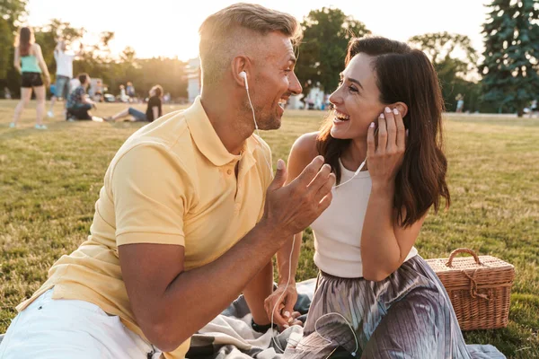 Heyecanlı orta yaşlı bir çiftin portresi. Yaz parkında oturmuş kulaklıkla gülüyor ve müzik dinliyor.