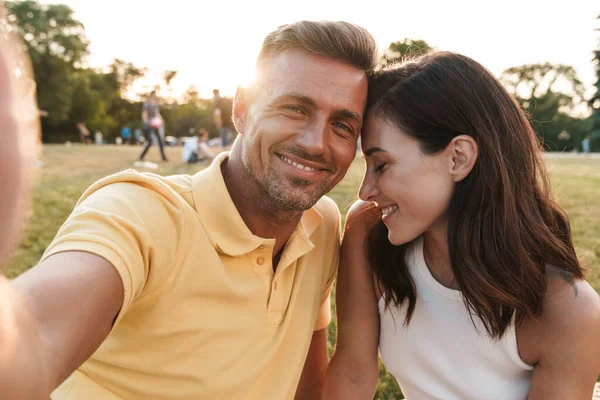 夏の公園に座っている間に自撮り写真や笑顔を撮る肖像画豪華な中年のカップルの男性と女性 — ストック写真