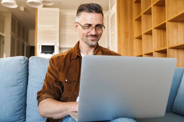 Imagem Homem Adulto Satisfeito Sorrindo Trabalhando Com Laptop Enquanto Sentado — Fotografia de Stock