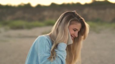 Yakışıklı sarışın bir kız kumsalda yürürken akıllı telefonuyla konuşuyor.