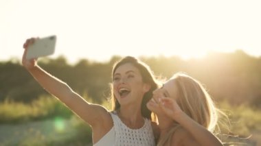 İki mutlu kız sahilde yürürken akıllı telefondan selfie çekiyorlar.