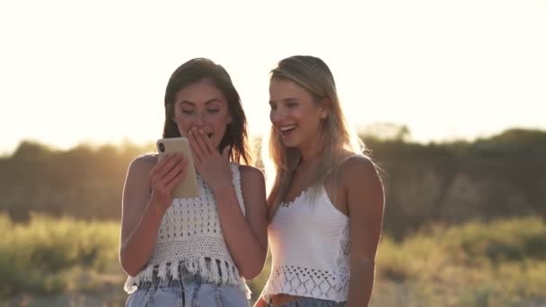Δύο Θετικά Κορίτσια Κοιτάζουν Φωτογραφίες Στο Smartphone Περπατώντας Στην Παραλία — Αρχείο Βίντεο
