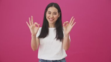 Gülümseyen bir kadın, pembe bir arka planda iki eliyle iyi bir hareket sergiliyor.