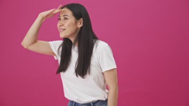 Neşeli bir kadın pembe bir arka planda izole edilmiş bir şey arıyor.