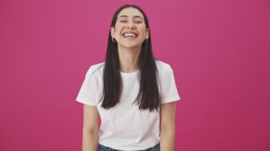 Gülümseyen neşeli bir kadın pembe bir arka planda tek başına duruyor.