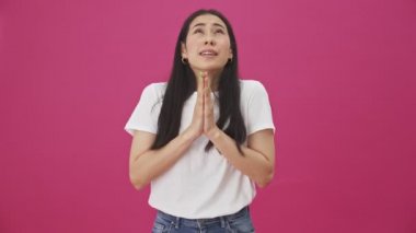 Duygusal genç bir kadın pembe bir arka planda tek başına el ele tutuşup dua ederken bir şey ister.