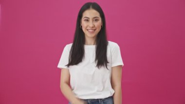 Gülümseyen genç bir kadın pembe bir arka planda gizli bir jest yapıyor.
