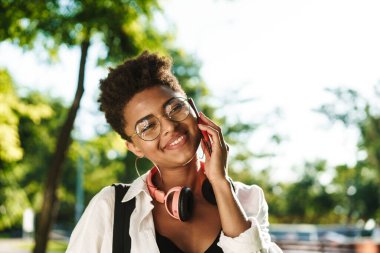 Genç, neşeli bir kadın açık havada telefonla çene çalıyor. Kapatın.