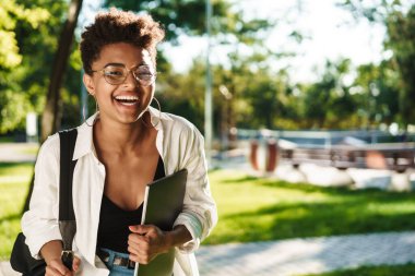 Elinde dizüstü bilgisayarla parkta gezen iyimser bir Afrikalı kadın görüntüsü