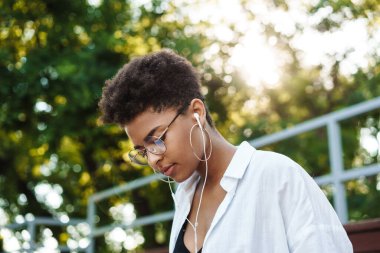 Ciddi bir Afrikalı kadının parkta oturmuş müzik dinlerken çekilmiş fotoğrafı.