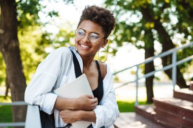 Parkta yürüyen çekici Afrikalı genç kız ders kitaplarını taşıyor.