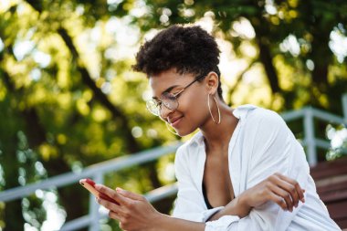 Gülümseyen Afrikalı bir kadının cep telefonuyla sohbet ederken parkta oturması