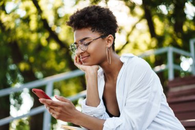 Mutlu Afrikalı bir kadının parkta oturmuş cep telefonuyla sohbet ederken fotoğrafı.