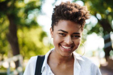 Parkta gezen iyimser gülümseyen Afrikalı kadın.