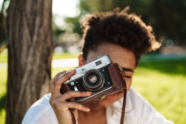 Parkta elinde kamerayla gülümseyen güzel bir Afrikalı kadının portresi. Kız fotoğraf çekiyor.