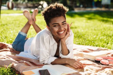 Mutlu gülümseyen Afrikalı bir kadının fotoğrafı. Parkta çimlerin üzerinde yatıyor.