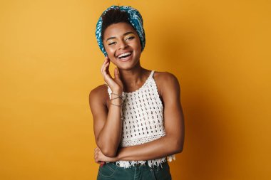 Kamera önünde poz veren ve gülen neşeli Afro-Amerikan kadın görüntüsü izole edilmiş sarı arka plan