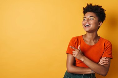 Afro-Amerikalı neşeli bir kadının parmağı bir yana, gülüşü izole edilmiş sarı arka plan.