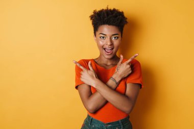 Şaşırmış Afrikalı Amerikalı kadının farklı tarafları işaret ettiği görüntüler izole edilmiş sarı arka plan.