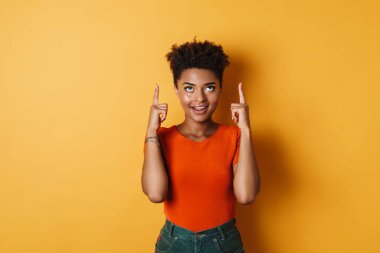 Neşeli Afro-Amerikan kadın tasviri. Parmakla işaret ediyor ve izole edilmiş sarı arka plan gülümsüyor.
