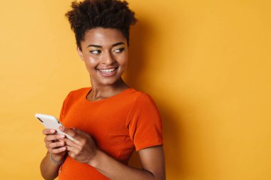 Gülümseyen ve cep telefonu kullanan mutlu Afro-Amerikan kadını görüntüsü.