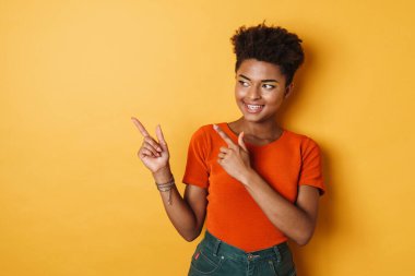 Afro-Amerikalı neşeli bir kadının, parmaklarını bir yana koyup, izole edilmiş sarı arka plan gülümsemesi.