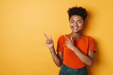 Afro-Amerikalı neşeli bir kadının, parmaklarını bir yana koyup, izole edilmiş sarı arka plan gülümsemesi.