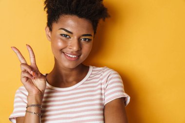 Afro-Amerikalı mutlu bir kadının barış işareti ve izole edilmiş sarı arkaplan gülümsemesi.