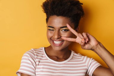 Afro-Amerikalı mutlu bir kadının barış işareti ve izole edilmiş sarı arka plan işareti.