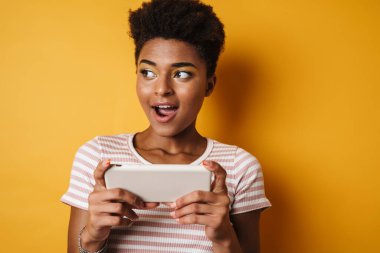 Cep telefonuyla online oyun oynayan Afrikalı Amerikalı bir kadının görüntüsü izole edilmiş sarı arka plan