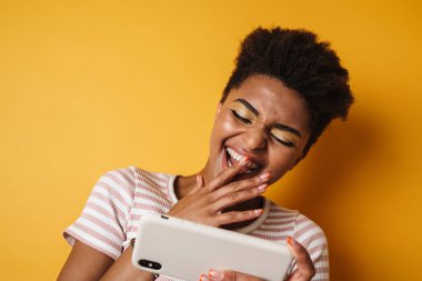 Neşeli Afro-Amerikan kadın görüntüsü cep telefonundan izole edilmiş sarı arka planda oyun oynuyor