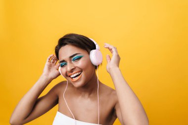 Sarı duvardan izole edilmiş kulaklıklarla müzik dinleyen neşeli Afrikalı Amerikalı kadın görüntüsü