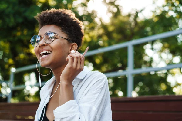 Parkta oturmuş müzik dinleyen iyimser bir Afrikalı kadının fotoğrafı.