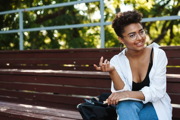 Genç Afrikalı öğrenci parkta bankta oturmuş ders kitabında bilgi arıyor.