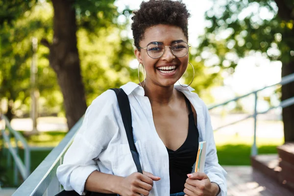 Parkta yürüyen çekici Afrikalı genç kız ders kitaplarını taşıyor.