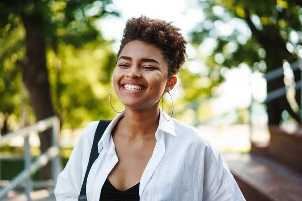 Mutlu, pozitif gülümseyen Afrikalı bir kadının parkta yürüdüğü bir fotoğraf.