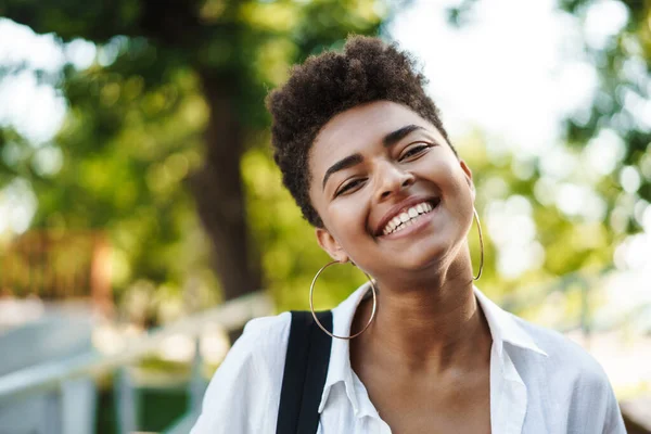 Mutlu, pozitif gülümseyen Afrikalı bir kadının parkta yürüdüğü bir fotoğraf.