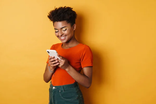 幸せなアフリカ系アメリカ人女性の笑顔と携帯電話を使用して黄色の背景を隔離 — ストック写真