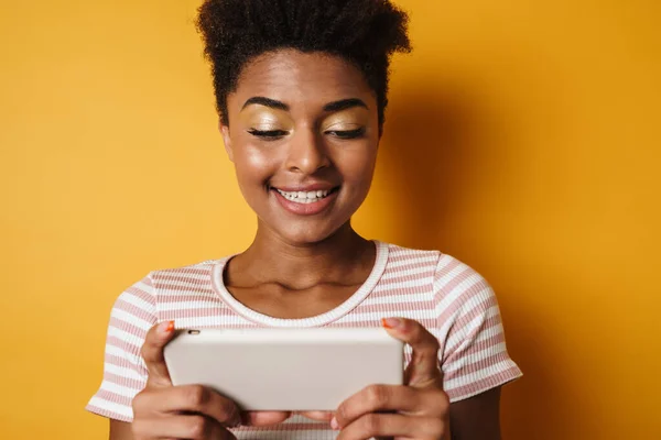 喜びアフリカ系アメリカ人女性のイメージは 携帯電話でオンラインゲームをプレイ孤立黄色の背景 — ストック写真