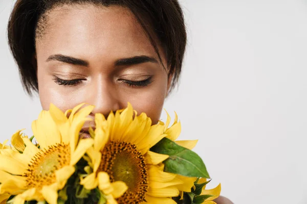 Beyaz arka planda izole edilmiş ayçiçekleriyle poz veren Afrikalı Amerikalı genç bir kadın.