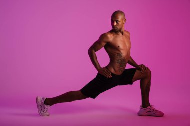 Pembe duvar arkasına izole edilmiş yakışıklı bir Afrikalı fitness sporcusunun görüntüsü esneme hareketleri yapıyor.