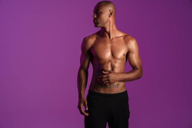 Mor duvarın üzerinden izole edilmiş, dövmeli, yarı çıplak, Afro-Amerikan bir adamın resmi.