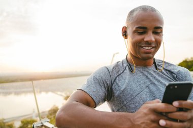 Açık havada, köprüde dinlenirken akıllı bir telefonla yazan Afrikalı genç bir adam.