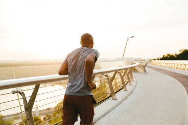 Genç bir Afrikalı koşucunun yan görüntüsü. Köprüde egzersiz yapıyor.