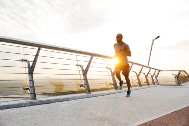 Genç bir Afrikalı koşucunun yan görüntüsü. Köprüde egzersiz yapıyor.