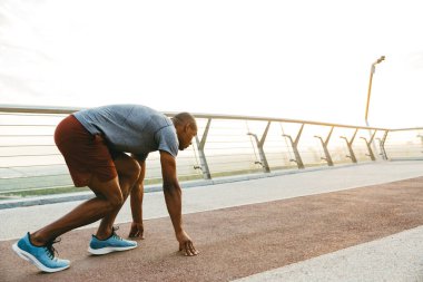 Genç bir Afrikalı koşucunun yan görüntüsü. Köprüde egzersiz yapıyor.