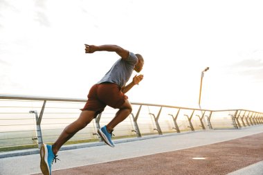 Genç bir Afrikalı koşucunun yan görüntüsü. Köprüde egzersiz yapıyor.