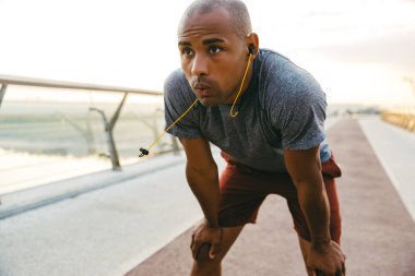 Rahatlamış Afrikalı sporcu köprüde kulaklıkla müzik dinlerken dinleniyor.