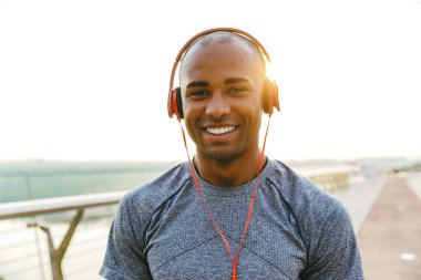 Afrika kökenli Amerikalı sporcu açık havada müzik dinliyor, köprüde duruyor.