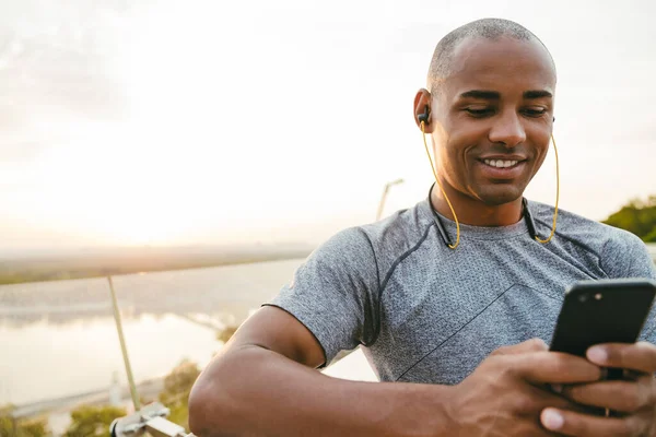Desportivo Jovem Africano Digitando Telefone Inteligente Enquanto Descansa Livre Ponte — Fotografia de Stock